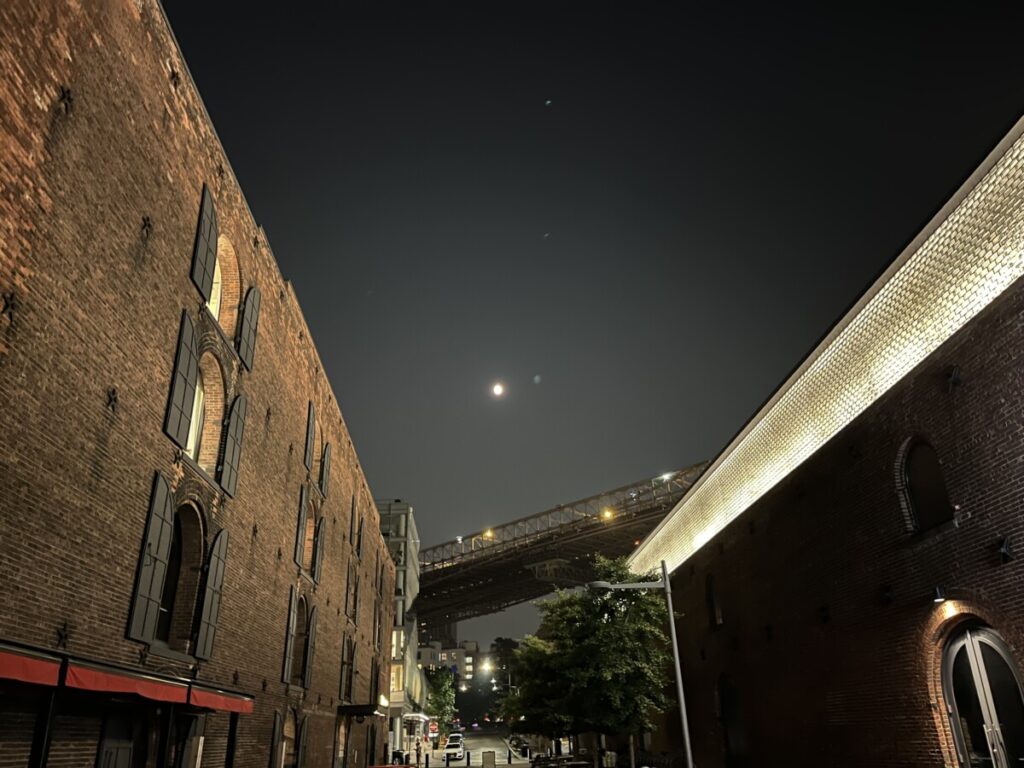 Image of Dumbo with the Brooklyn Bridge in the background dividing the night sky and the buildings, Taken at night.