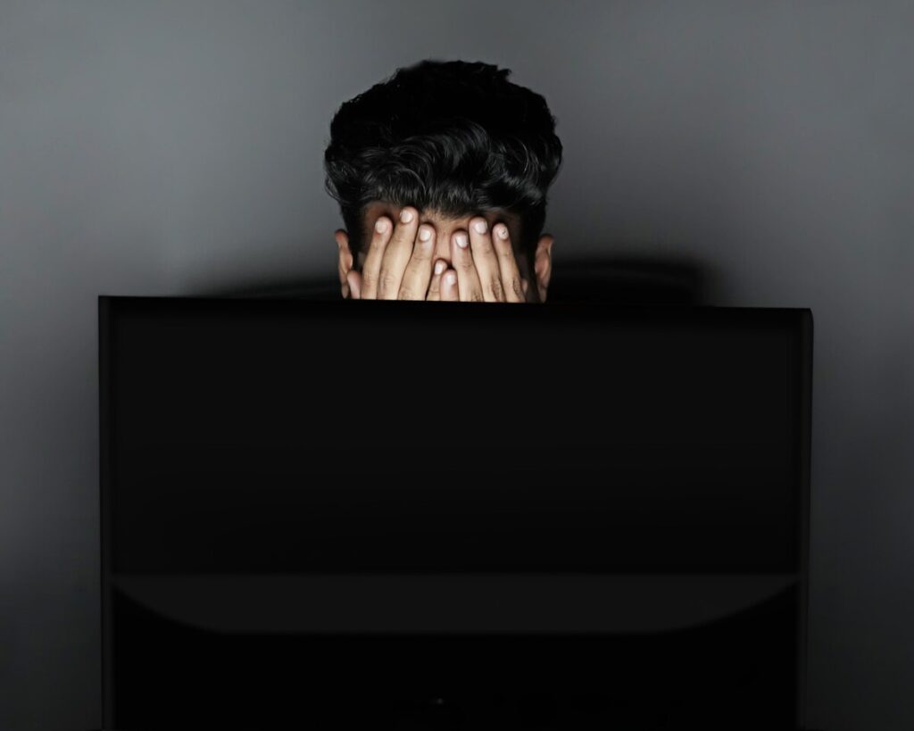 Person infront of computer screen stressed out with their hands covering their face