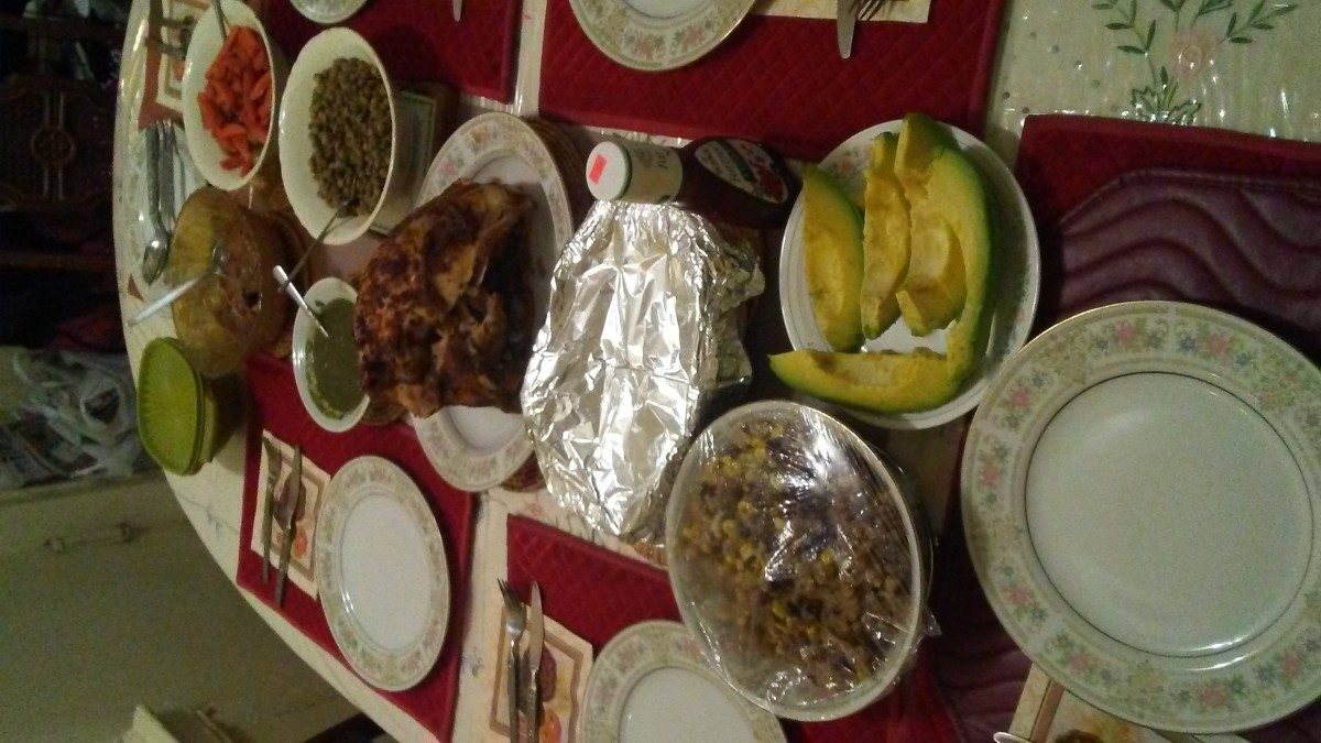 a table featuring a roasted turkey, sliced avocados, callaloo, split pea gravy, roasted carrots and brussel sprouts, and stuffing