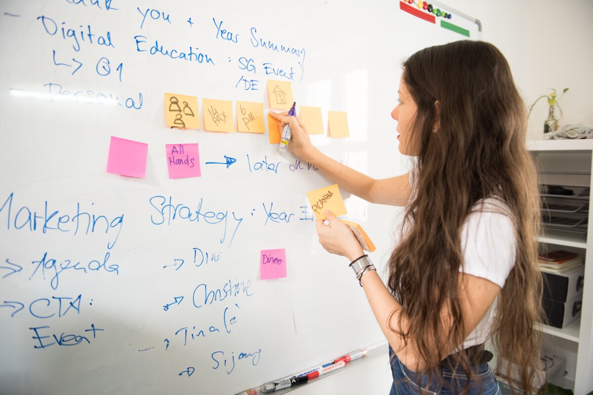 This is an image of a girl placing a post it on a board and she appears to be brainstorming ideas