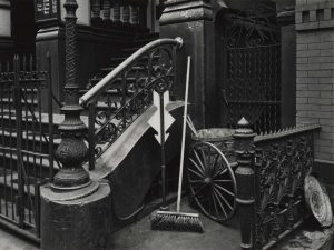 Black and white photograph of a stoop with a broom and arrow sign