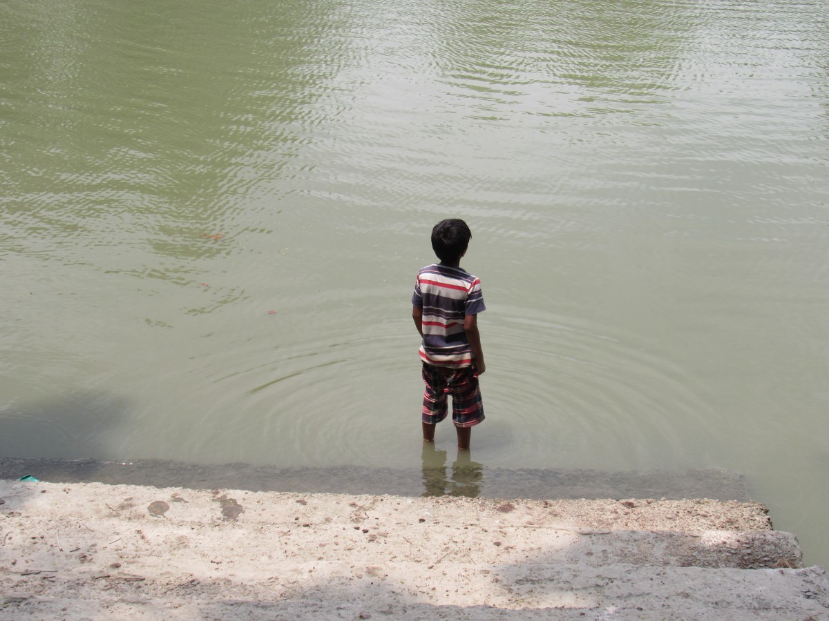 Boy standing at the edge of a pond.