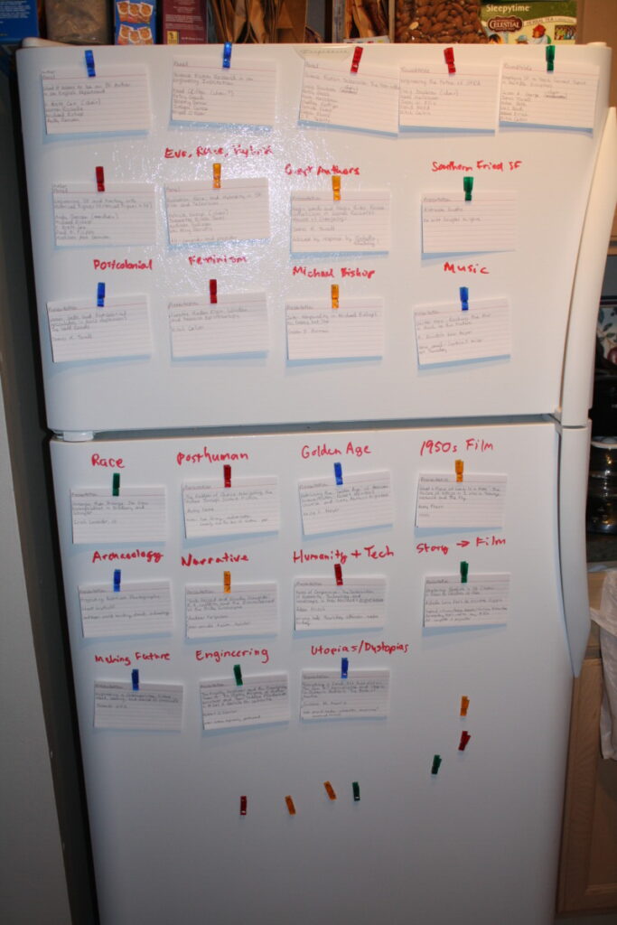 Planning a conference schedule using notecards and dry erase markers on a white refrigerator.