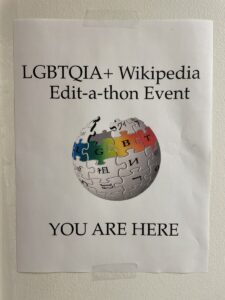 A white background image with a Wikipedia Globe in the middle that highlights the word 'LGBT' in a rainbow color. On top of the globe, there is a text that says 'LGBTQIA+ Wikipedia Edit-a-thon Event.' Below the globe is a text that says, 'You Are Here.'