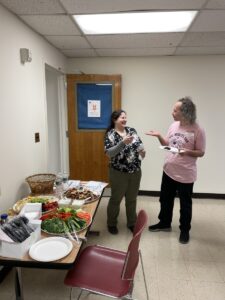 An image of two attendees talking to one another next to a table filled with catered food. 