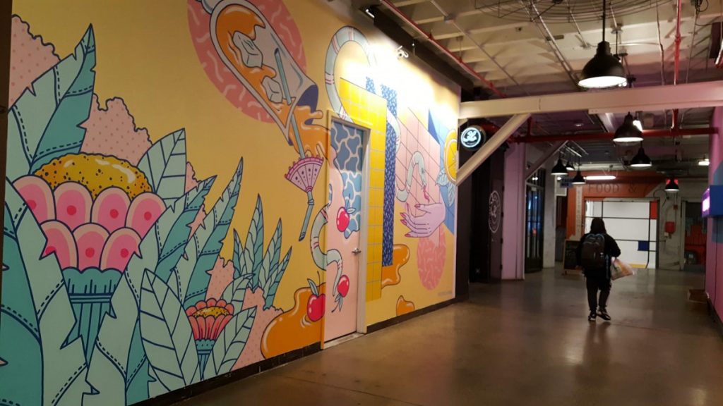 Within the Industry City Food Hall is a work of art featuring an artist - Photo credit by Laura Ng