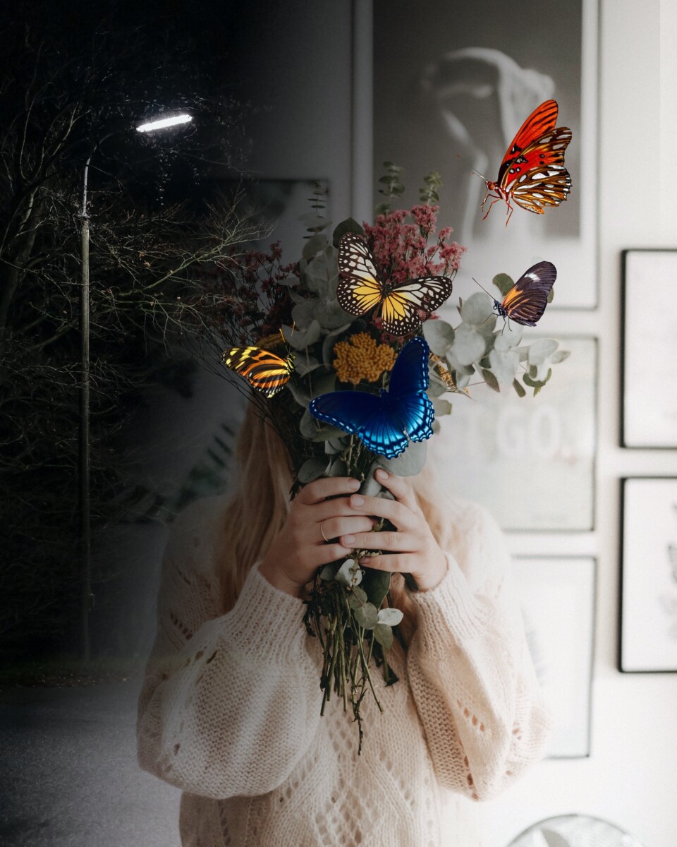 A person holding flowers with butterflies flying around her faceDescription automatically generated