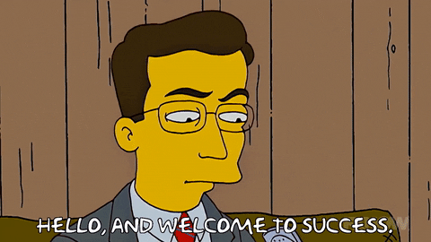 A character from the Simpsons wearing glasses and a necktie speaking into an old-fashioned flip phone saying, "Hello, and welcome to success."