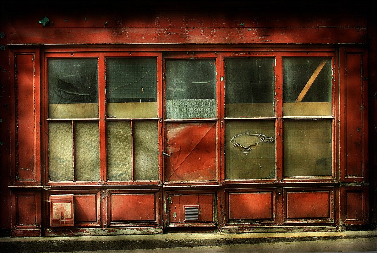 Color photograph of a storefront painted red with several windows and mottled shadows