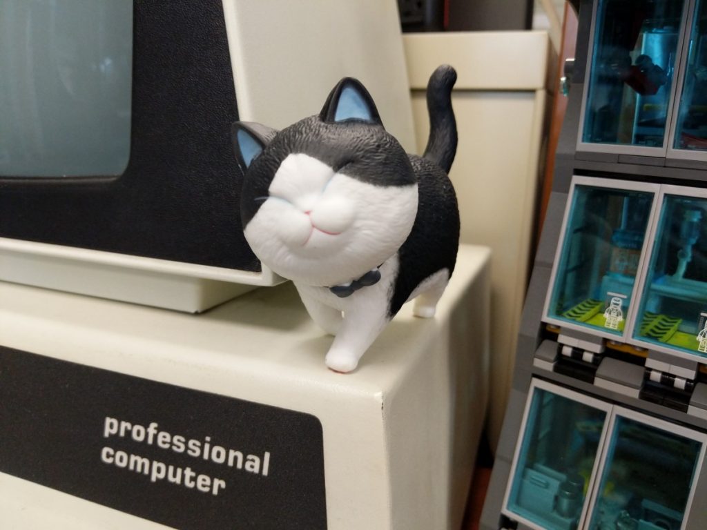 Photo of a black-and-white plastic cat with their head cocked atop a beige box with the words "professional computer" displayed in white text on a black background