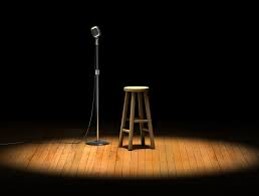 A mic and a stool stand on an empty stage.