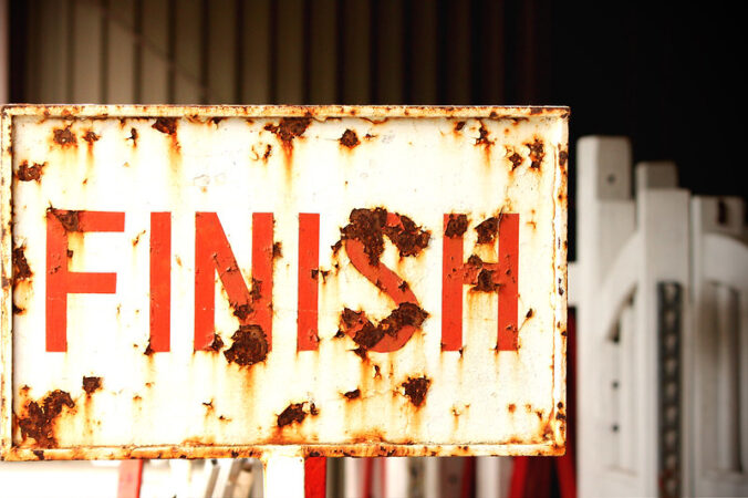 A white sign that reads FINISH in red letters, with rust spots throughout.