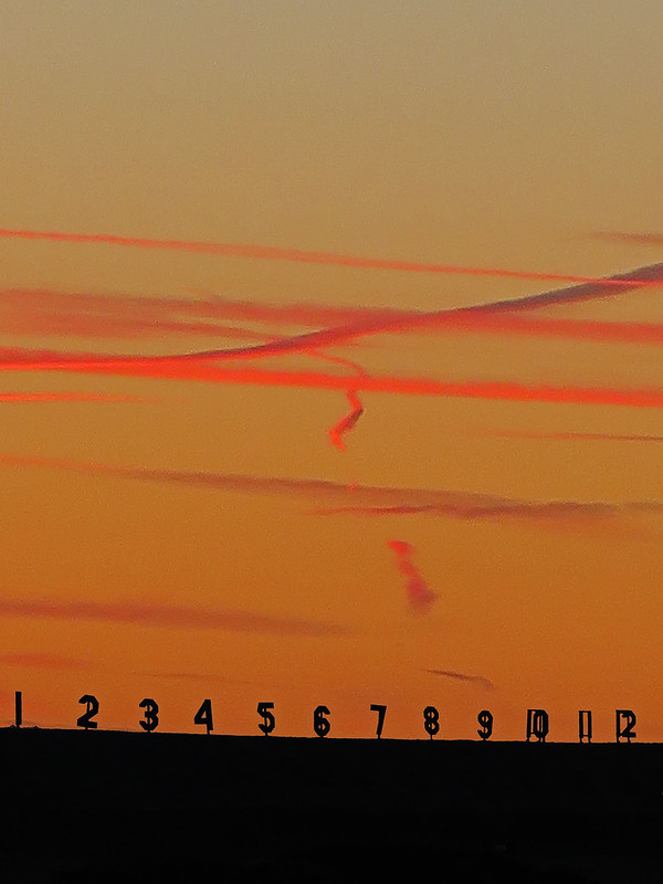 red trails in an orange sky, with numbers 1 through 12 along the horizon line.