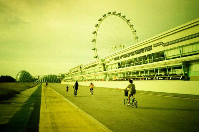 yellow-cast image of singaopre grand prix with a few bicyclists and a ferris wheel in the distance