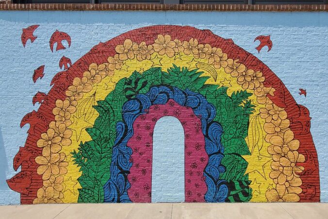 mural of a rainbow with various shapes and objects, including birds flying out of the red band