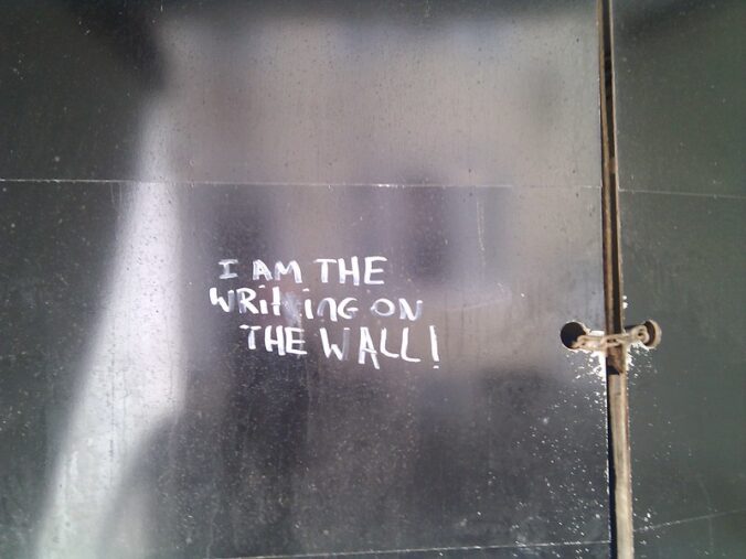metal wall with white letters that read "I AM THE WRiTiNG ON THE WALL"