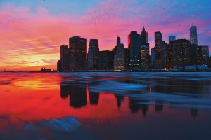 a colorful sunset on the water, by a city skyline