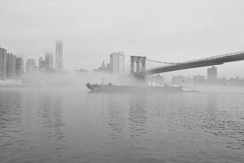 fog covering a ship sailing under a bridge