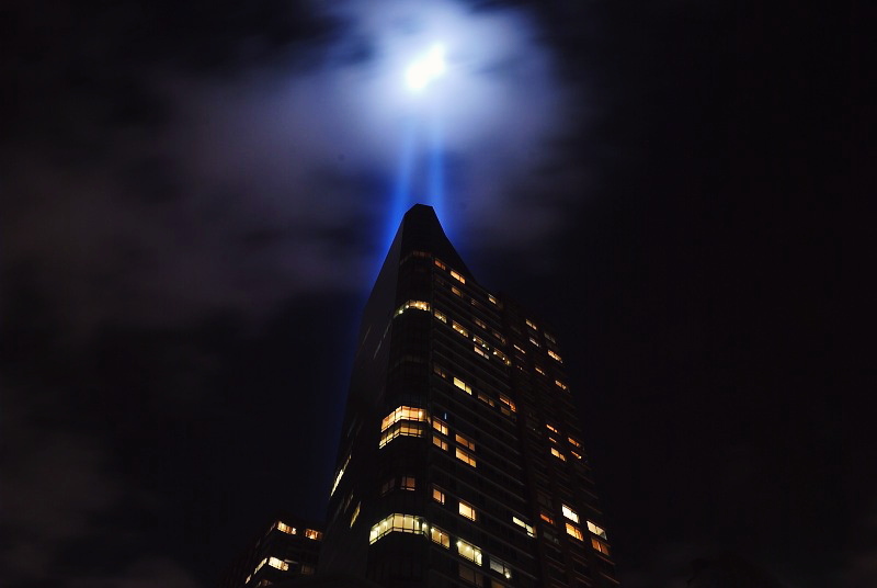 a city building at night with a beam of blue light coming out of the top