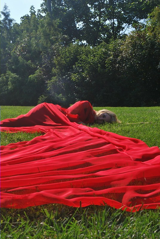 a woman lying on a field, wrapped in red fabric