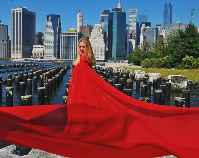 a woman wrapped in moving red fabric in front of a pier