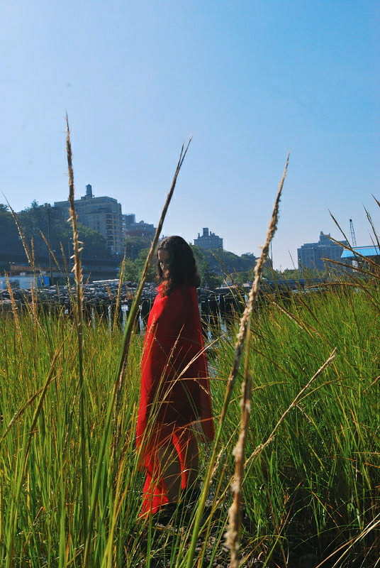 a woman wrapped in red fabric, standing in a field