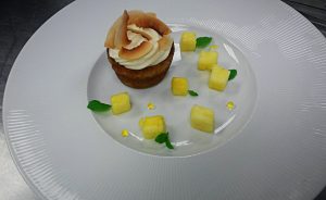 a cupcake covered with toasted coconut chips and plated with diced mangoes