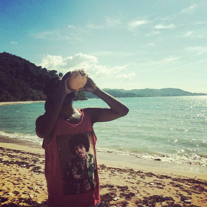 a person on a beach, drinking from a coconut shell