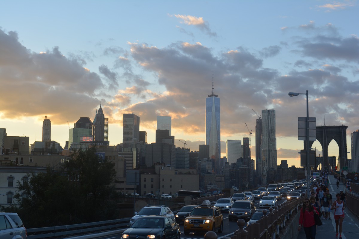 a city skyline in front of a sunset sky, with cars on a bridge