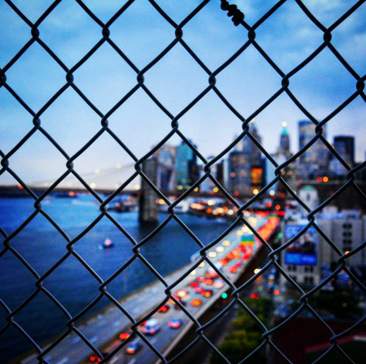 the view of the city from a bridge, through a wire mesh fence