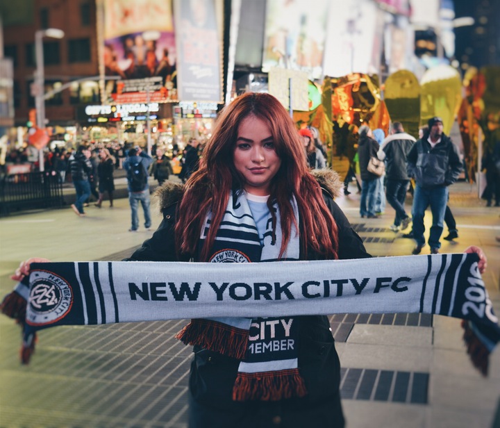 a young woman with long hair holding a "New York City FC" sign