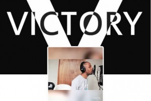 a man wearing large black headphones, in front of an image of the word "Victory"