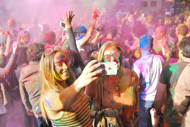 two young women taking a selfie in a crowd covered in paint