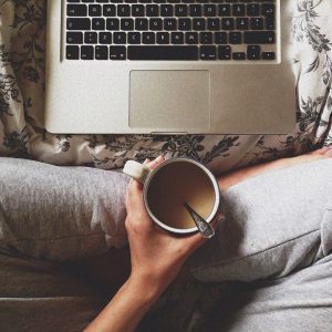 a woman's lap, a coffee cup in her hand, and a laptop keyboard