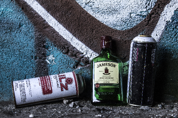 two paint cans and a whiskey bottle on the ground, against a turquoise wall