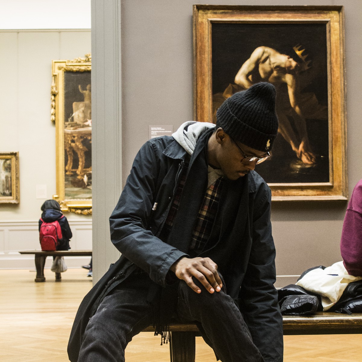 a man in glasses and a beanie hat in front of a painting
