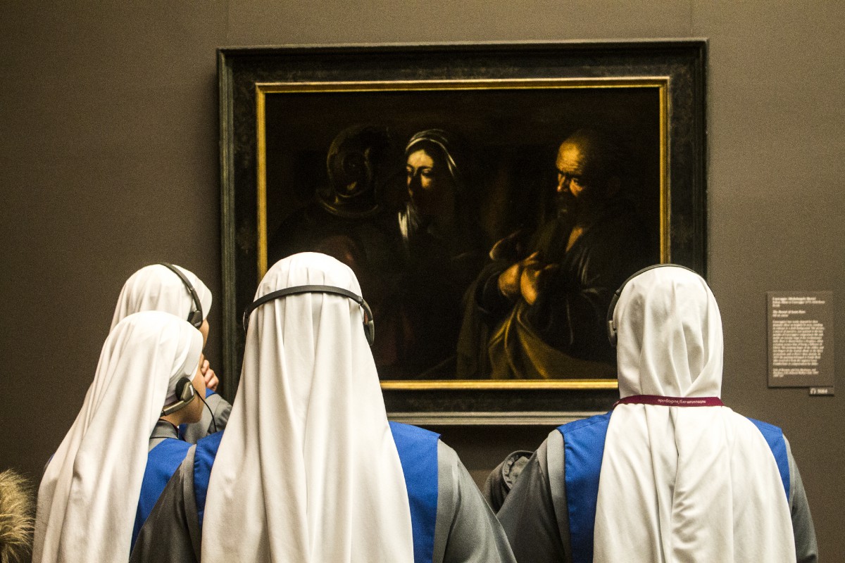 three nuns in white habits looking at a painting