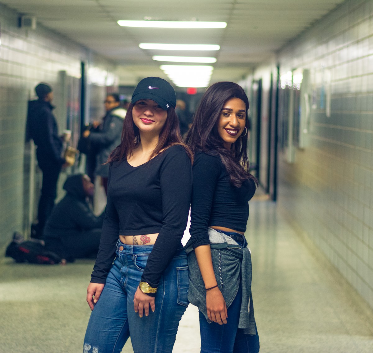 two young women back to back in jeans, in a hallway