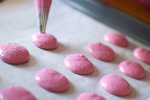 macarons being piped on a sheet pan