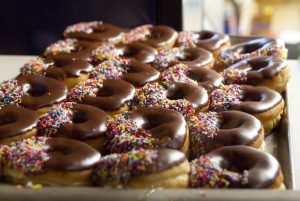 a tray of chocolate glazed donuts covered with rainbow sprinkles