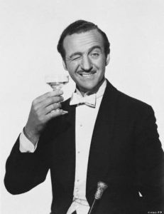 a man in suit and bow-tie holding a martini glass and winking