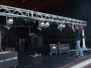 a person hanging a light off of a horizontal truss onstage.
