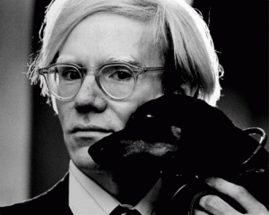 Andy Warhol glaring into the distance while holding a dog