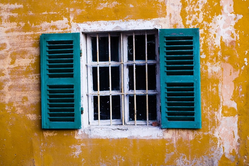 white-framed window with turquoise shutters on an ochre building.