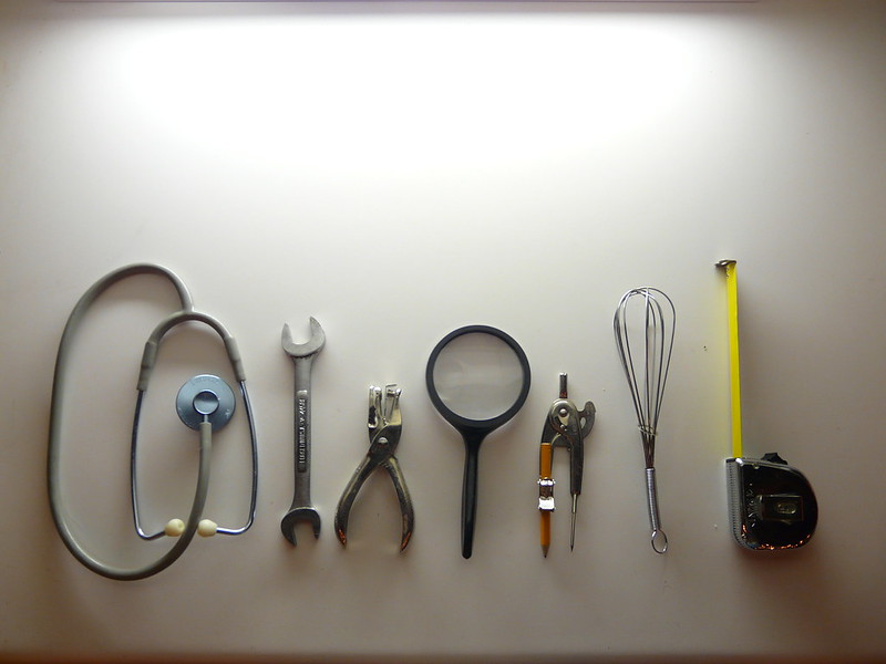 various tools: a stethoscope, wrench, pliers, magnifying glass, drawing compass, whisk, and tape measure