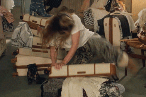 animated gif of a woman sitting on an over-stuffed suitcase to try and close it